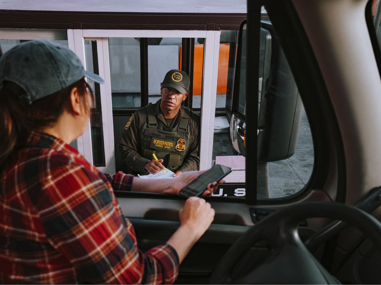 Uber Freight Navigating tariff disruptions Truck driver talking to border control agent and referencing the Uber Freight carrier app on their phone